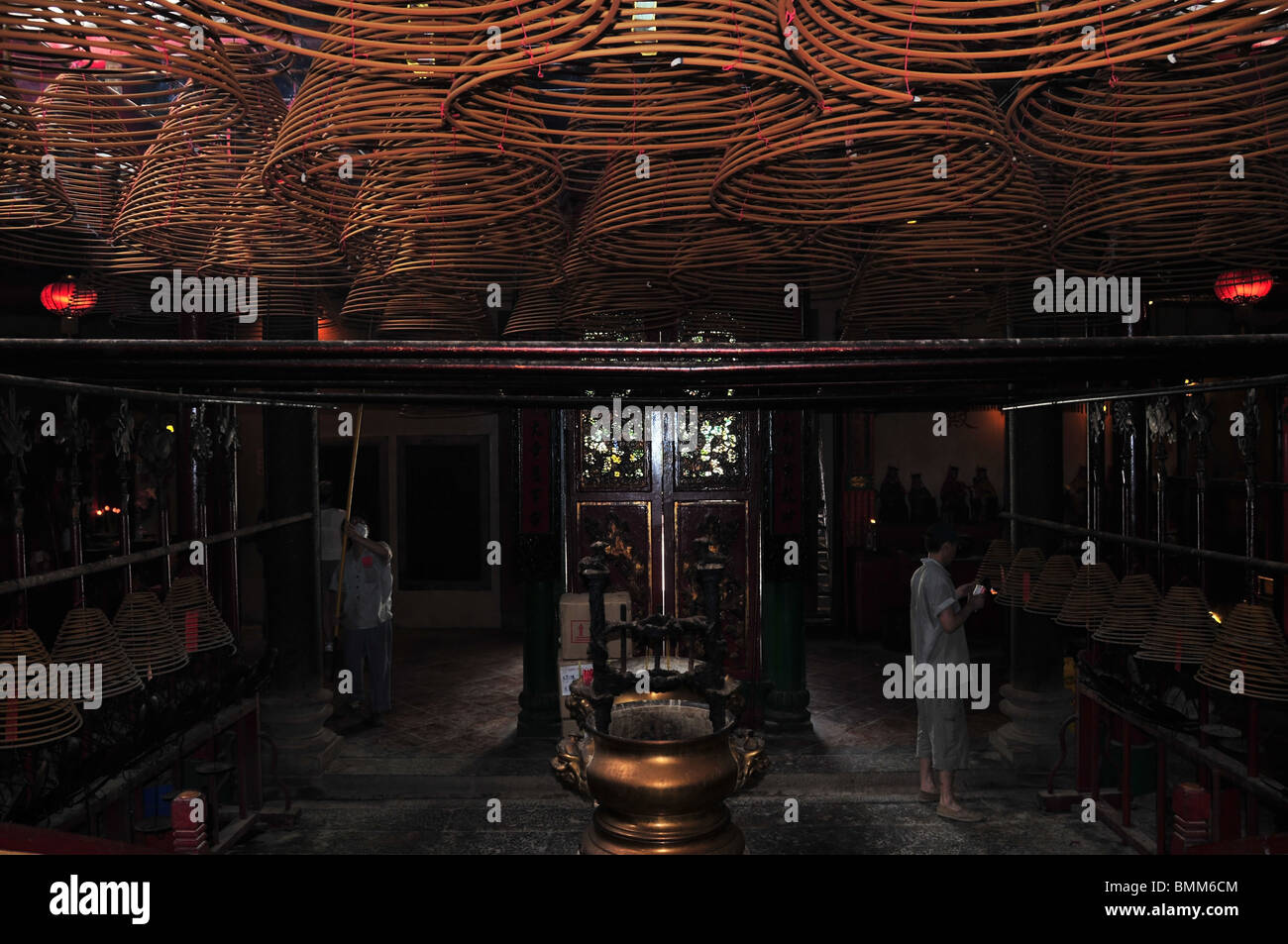 Incense cone attendants, with blow torch and wooden lifting pole, working in the interior of the