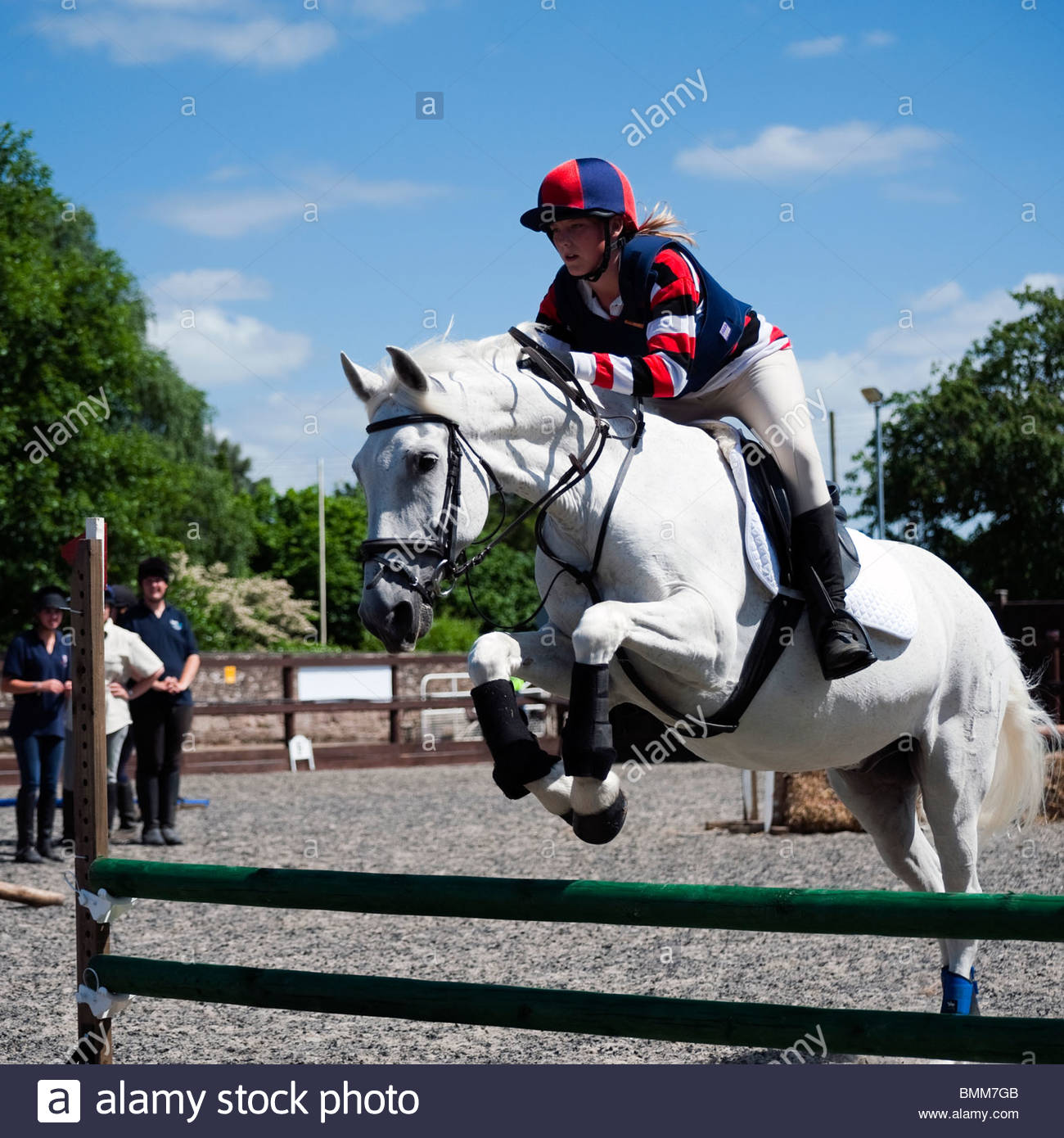 Show jumping with a white horse in an equine arena. Teenage girl Stock