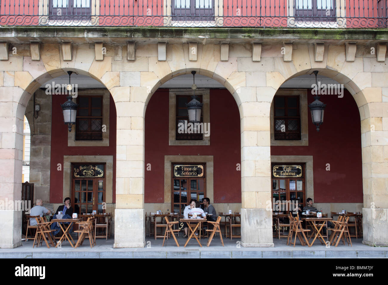 Cafe under arches of colonnade of Plaza Major, Gijon, Asturias, with wooden tables and red painted stonework Stock Photo