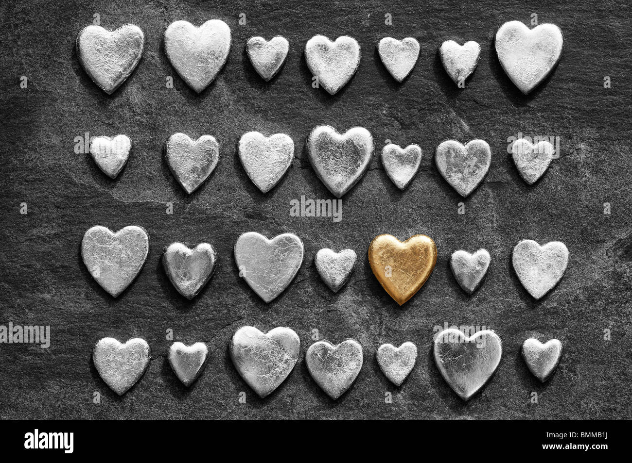 Gold heart shape against slate background with monochrome hearts Stock Photo