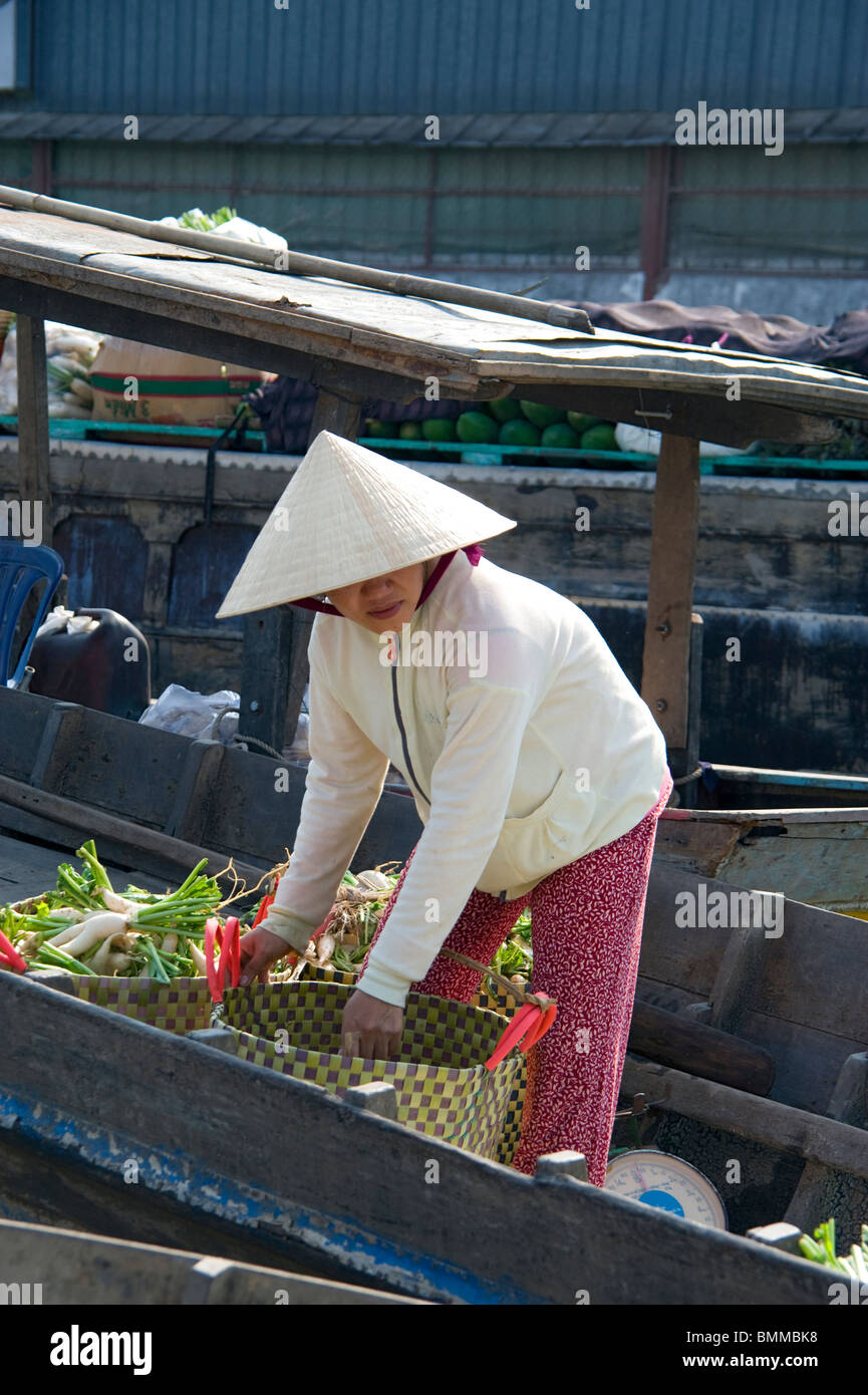 A Vietnamese woman wearing a traditional conical hat loading baskets on her boat at the floating market in Cai Rang, Vietnam Stock Photo