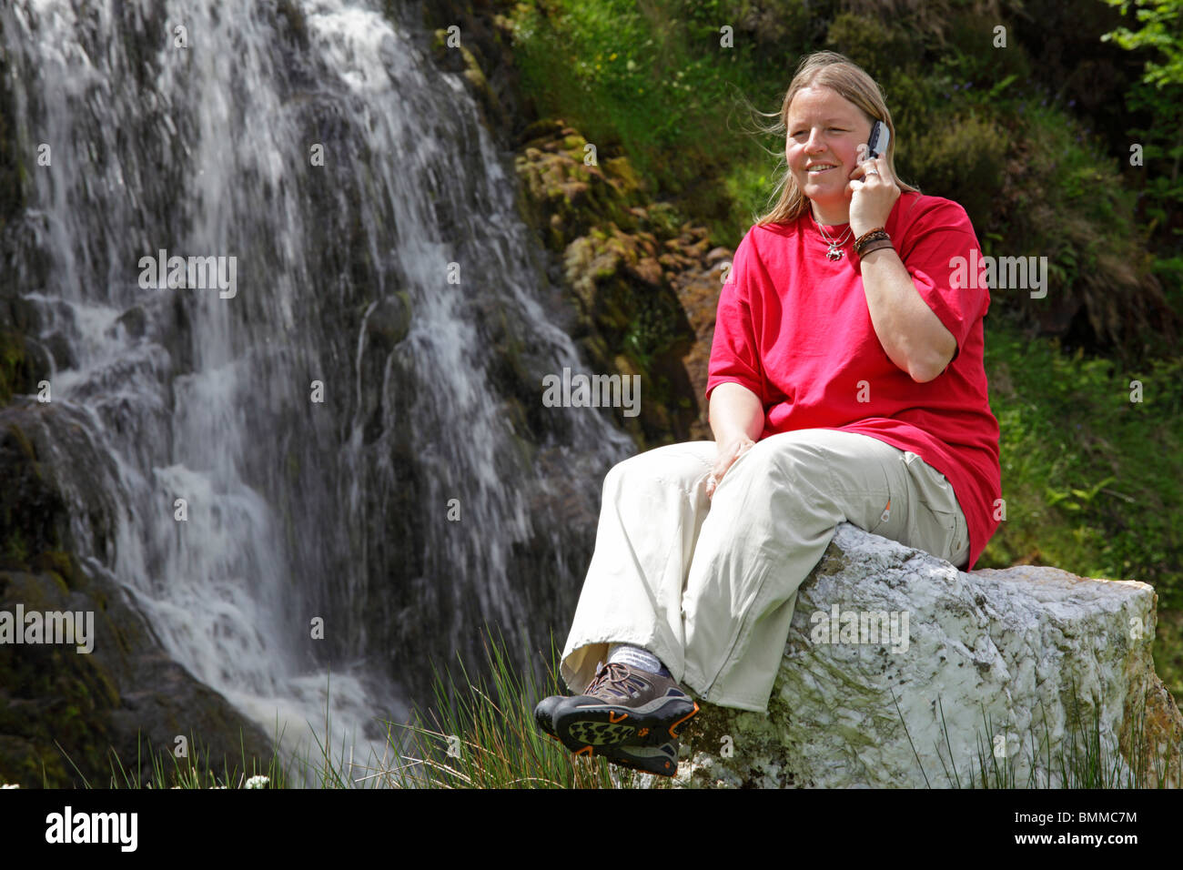 young woman talking on her mobile phone in front of a waterfall near Ardara, Co. Donegal, Republic of Ireland Stock Photo