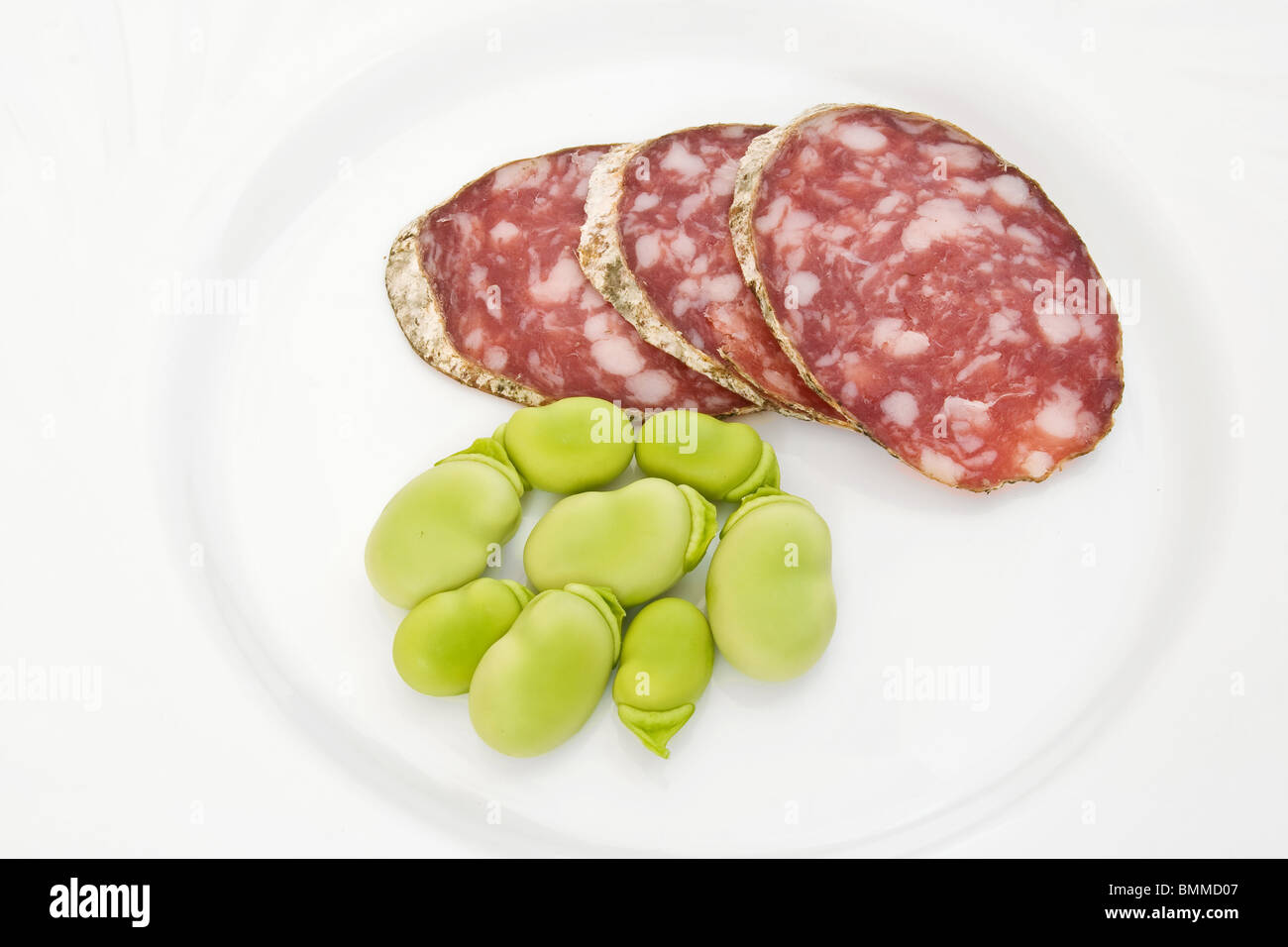 Three salami slices with fava beans on a white dish Stock Photo