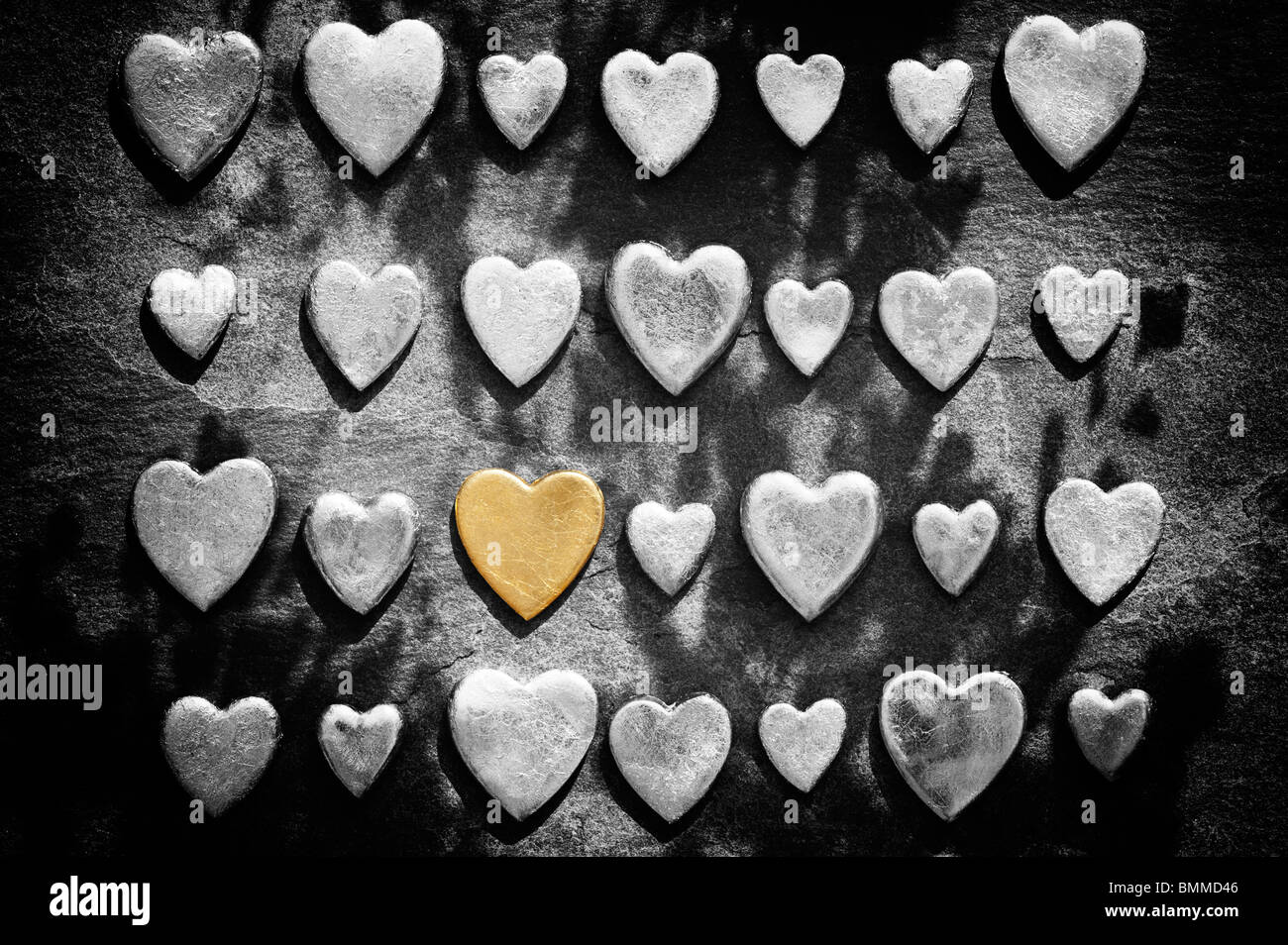 Gold heart shape against slate background with monochrome hearts in light and shade Stock Photo