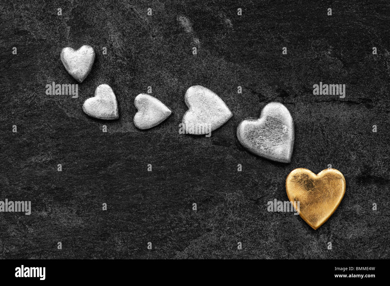 Gold heart shape against slate background with black and white hearts Stock Photo