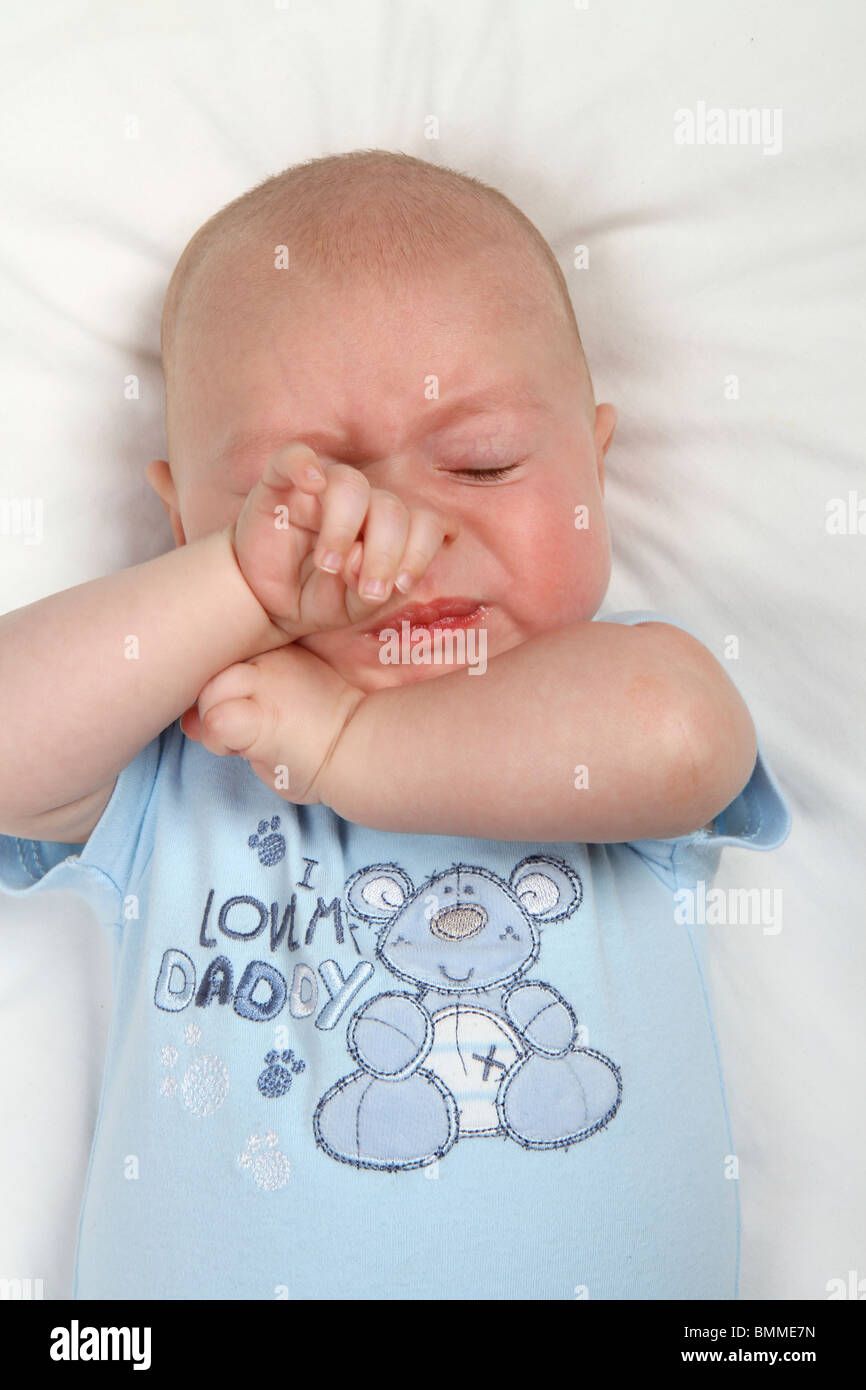 Caucasian baby boy rubbing his face with hands and screwing up face