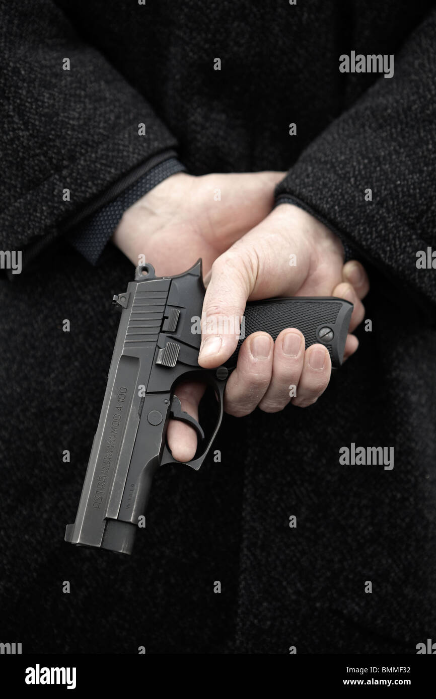 Man holding loaded gun behind his back Stock Photo