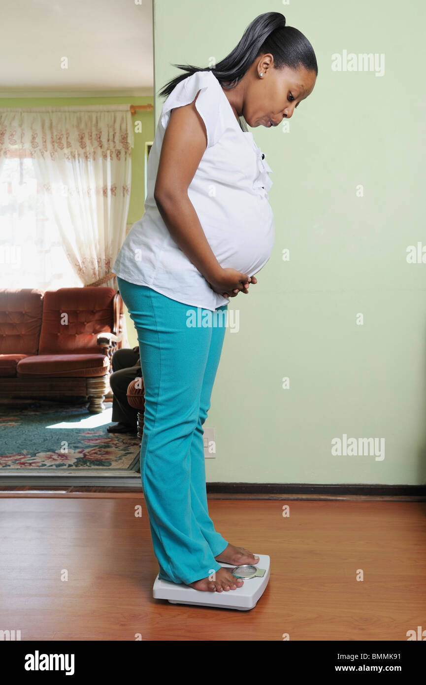 Pregnant young woman weighing herself on scale, Cape Town, Western Cape Province, South Africa Stock Photo
