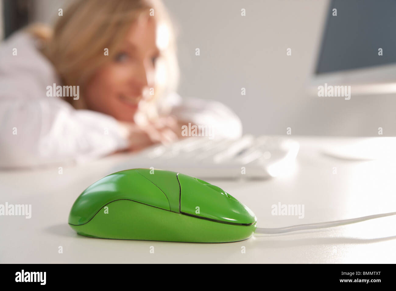 Green mouse on office desktop with woman Stock Photo