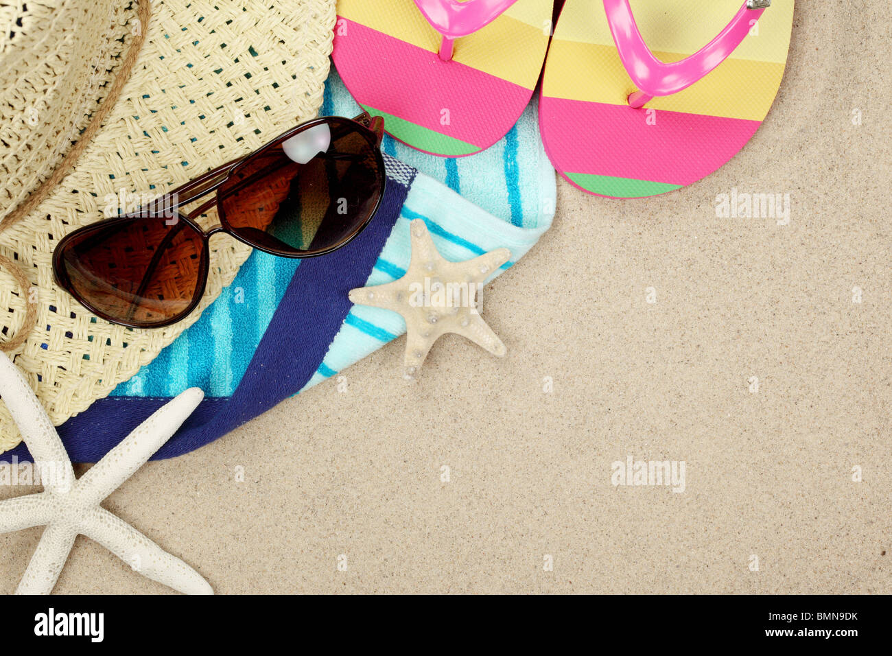 Colorful summer beachwear, flip flops, towel, hat, sunglasses and starfish on sand beach. Stock Photo