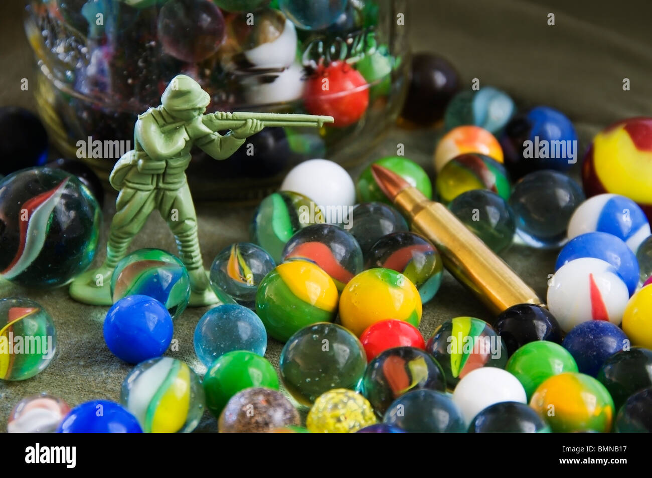 Collection of multicolored marbles, a green plastic toy soldier action figure and a rifle round. Stock Photo