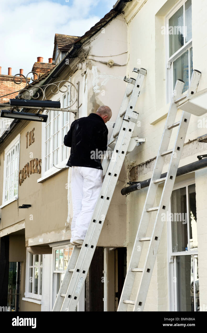 Man up ladder, a painter and decorator decorating the outside wall ...