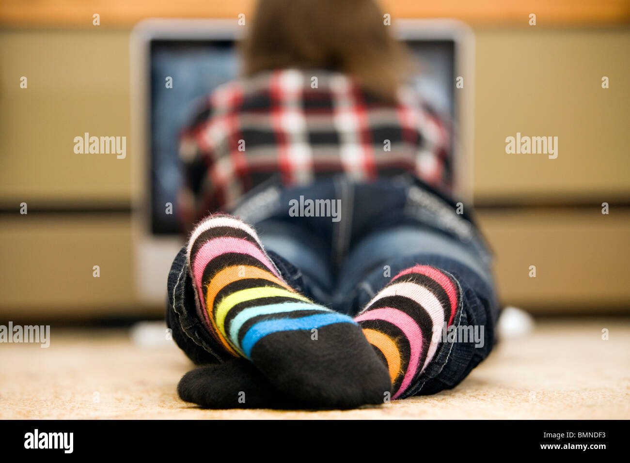 Teenager lies on floor in front of her computer. Stock Photo