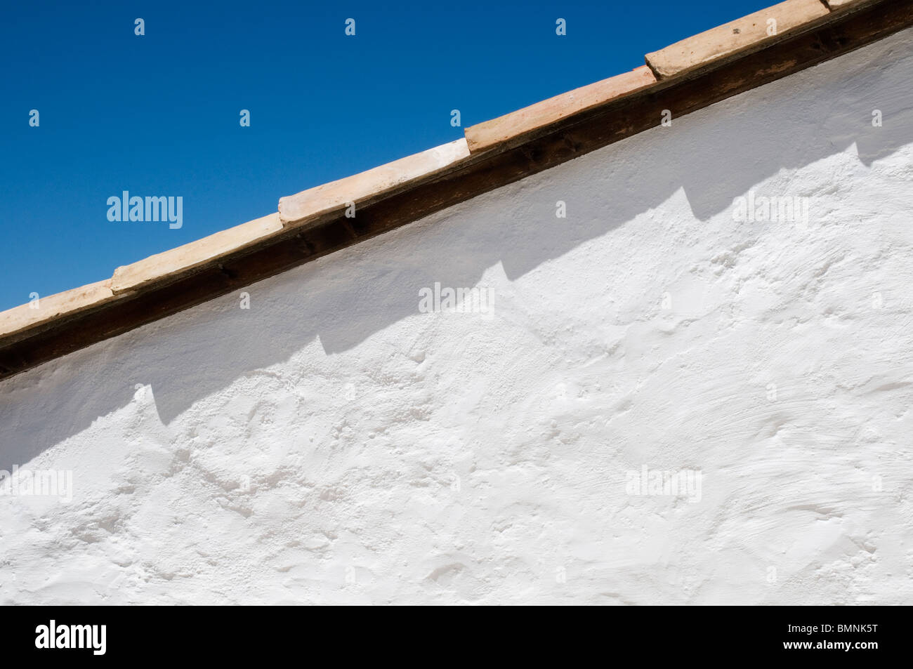 Whitewashed wall and clay roof tiles against a bright blue sky Stock Photo