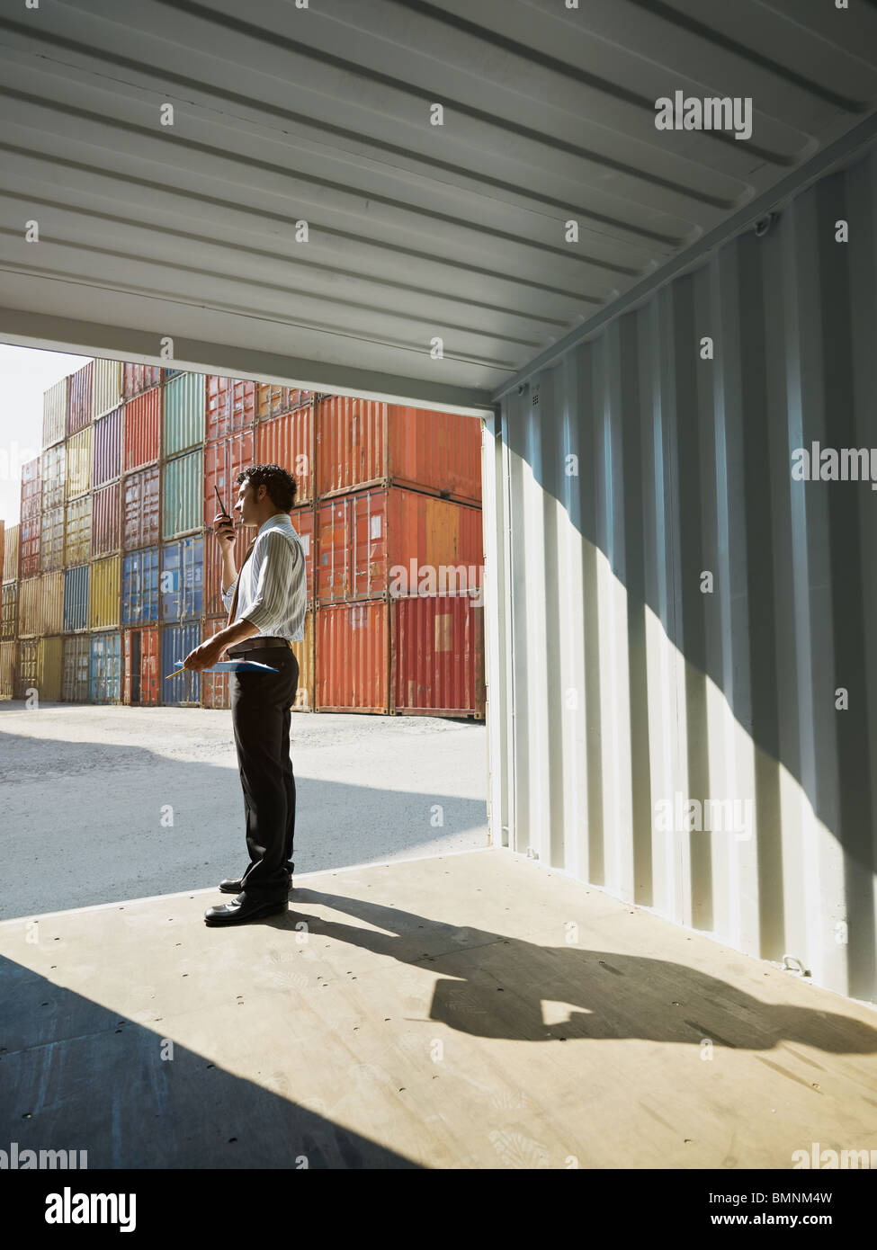 portrait of mid adult businessman standing near cargo container and talking . Vertical shape, side view, copy space Stock Photo