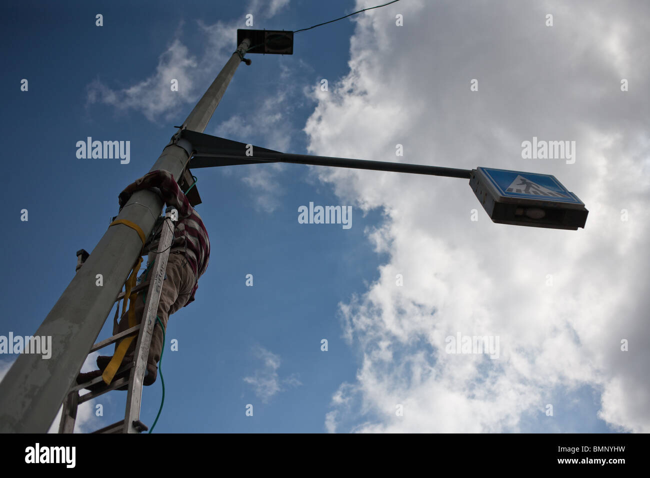 Electrician Standing on Ladder and Working on a Light Pole Stock Photo