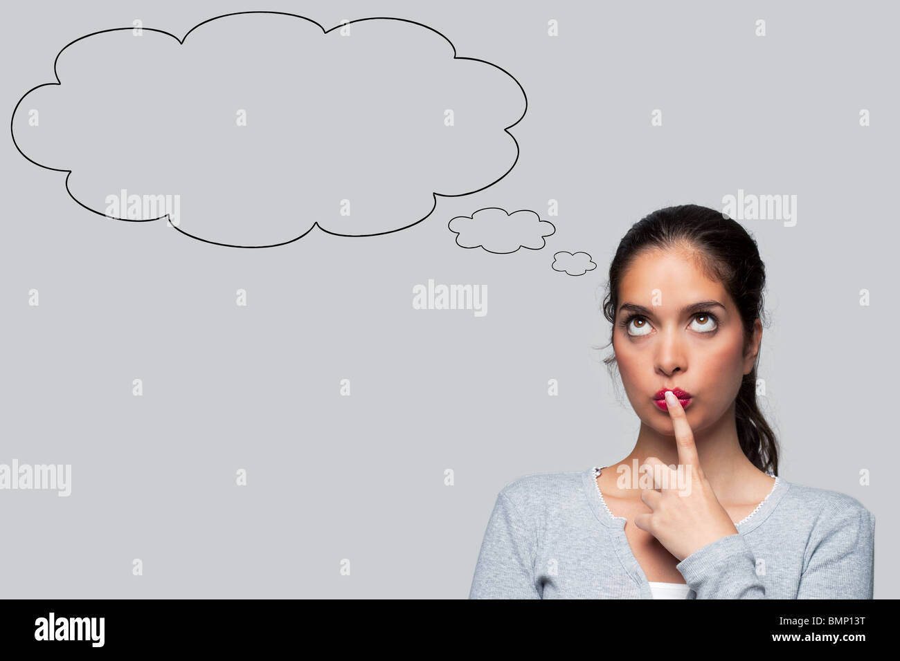 Woman with big brown eyes looking upwards thinking with blank thought bubbles above her head, isolated on white background. Stock Photo