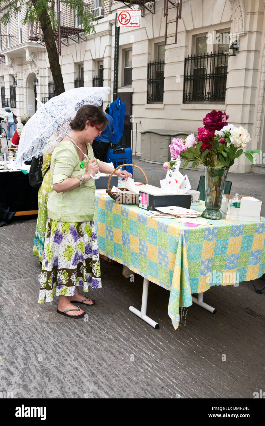 woman shaded by pretty lace parasol shops for novelty cards at west side Manhattan block annual flea market New York City Stock Photo