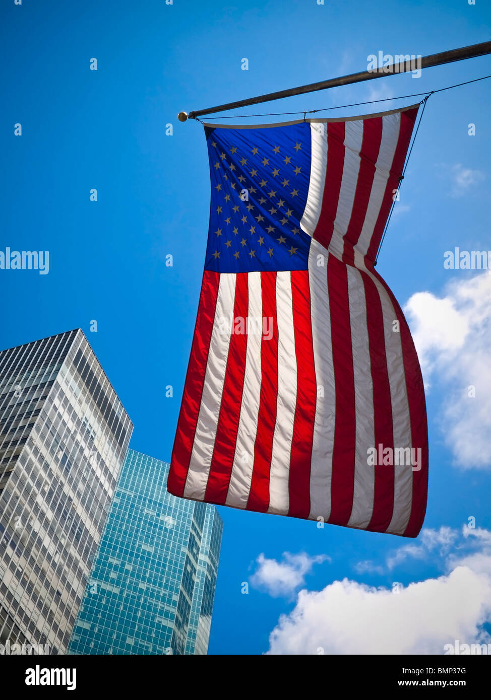 An American flag waving against two skyscrapers and a blue sky. Stock Photo