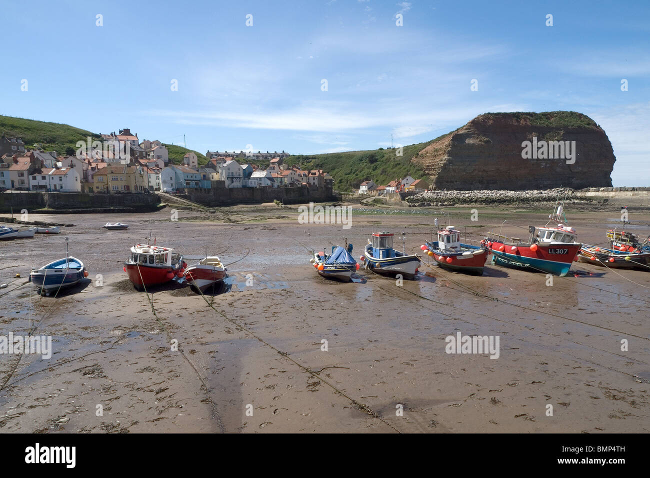A line of fishing boats lie on the sand at low tide in Staithes Harbour ...