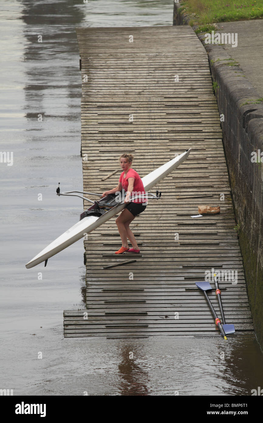 A girl struggles to lift a single scull rowing boat out of the river in