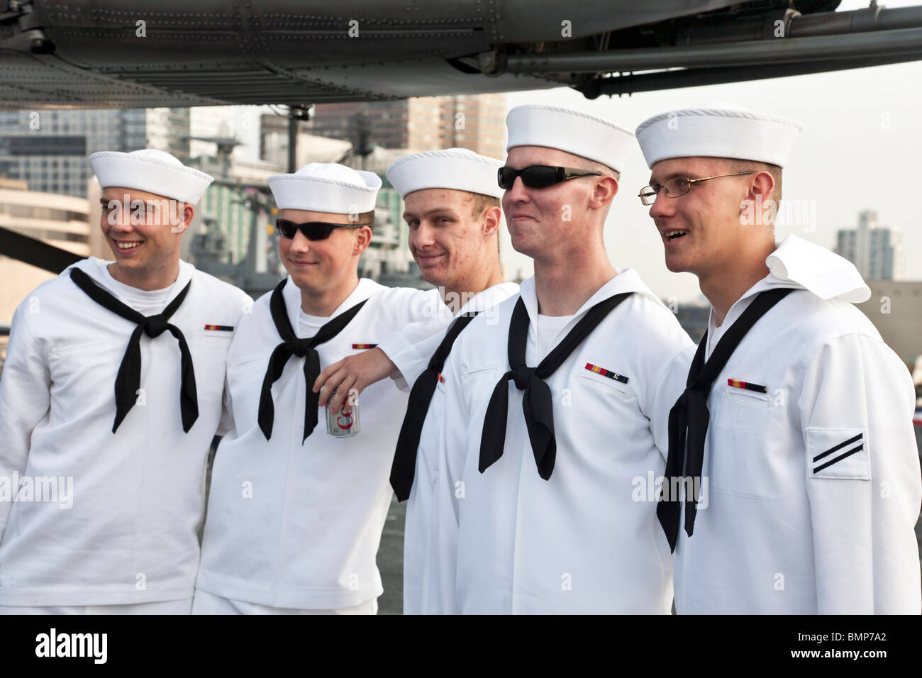 five smiling young sailors in dress whites pose for visitors on flight deck of USS Iwo Jima during fleet week in New York City Stock Photo