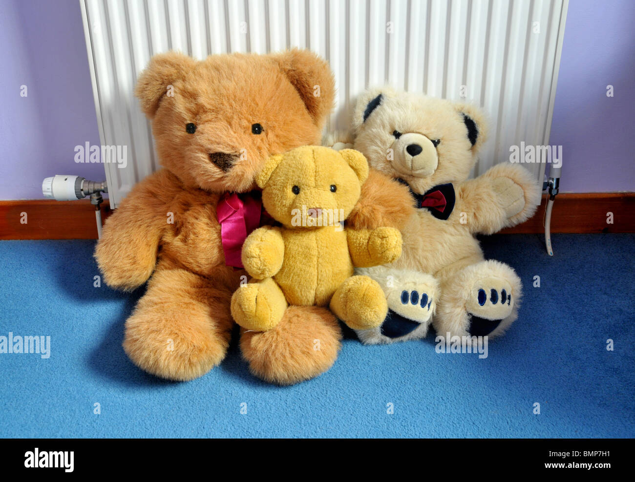 A family group of toy teddy bears sitting on the carpet and leaning against a radiator. Stock Photo