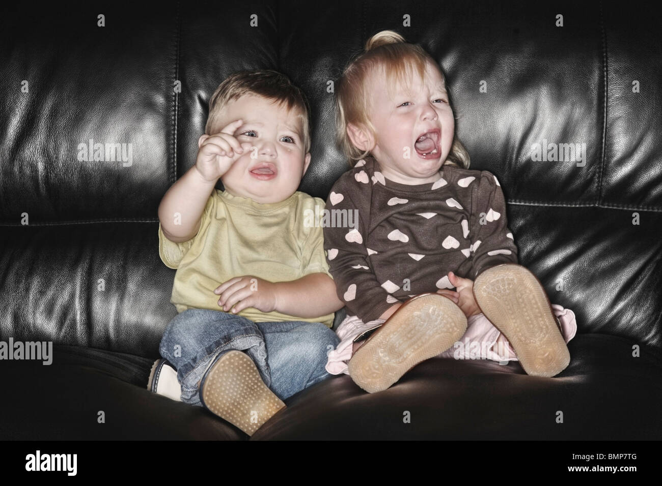 Edmonton, Alberta, Canada; Two Young Children Sitting On The Couch Together And Crying Stock Photo
