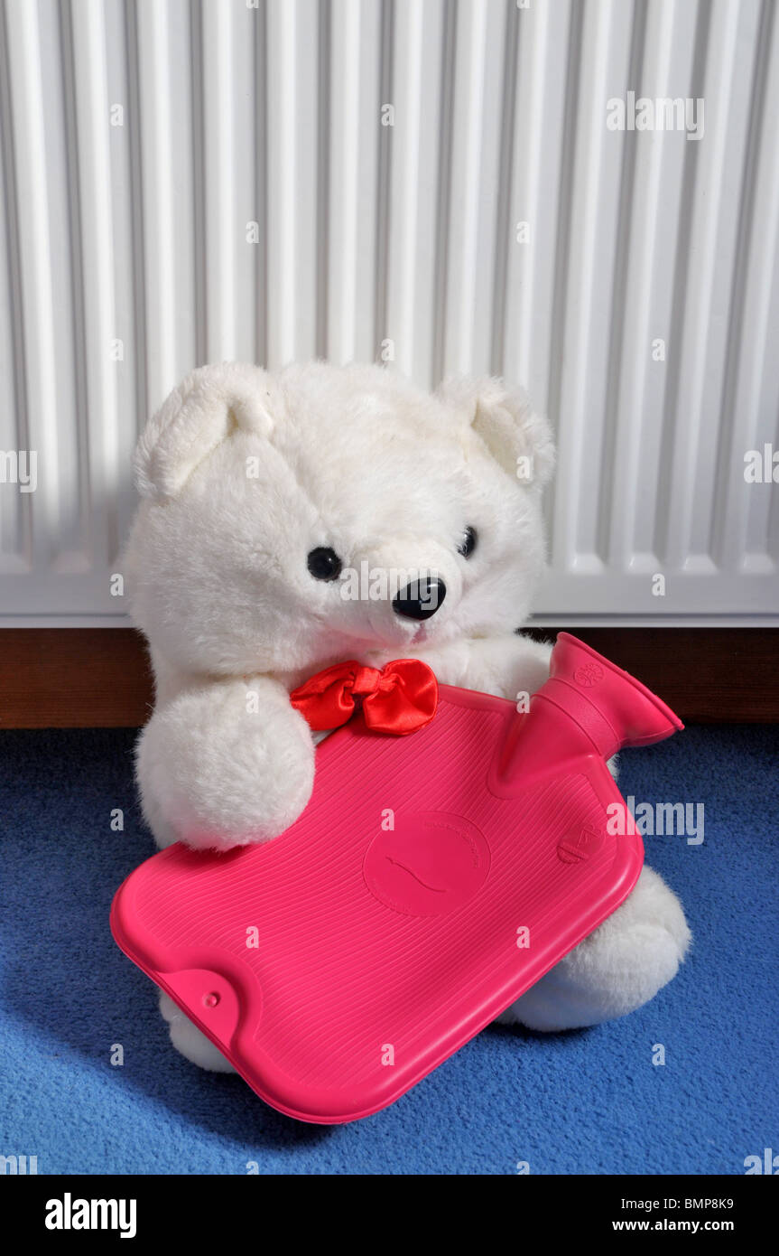 A white seated teddy bear leaning against a radiator holds a hot water bottle. Stock Photo