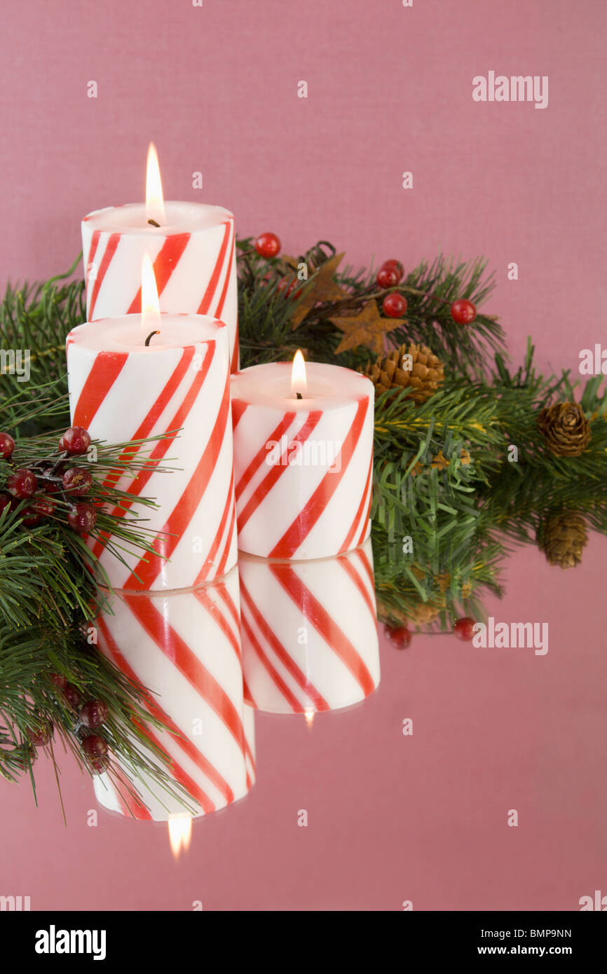 three red and white striped Christmas candles on a reflective wine colored background with copyspace Stock Photo
