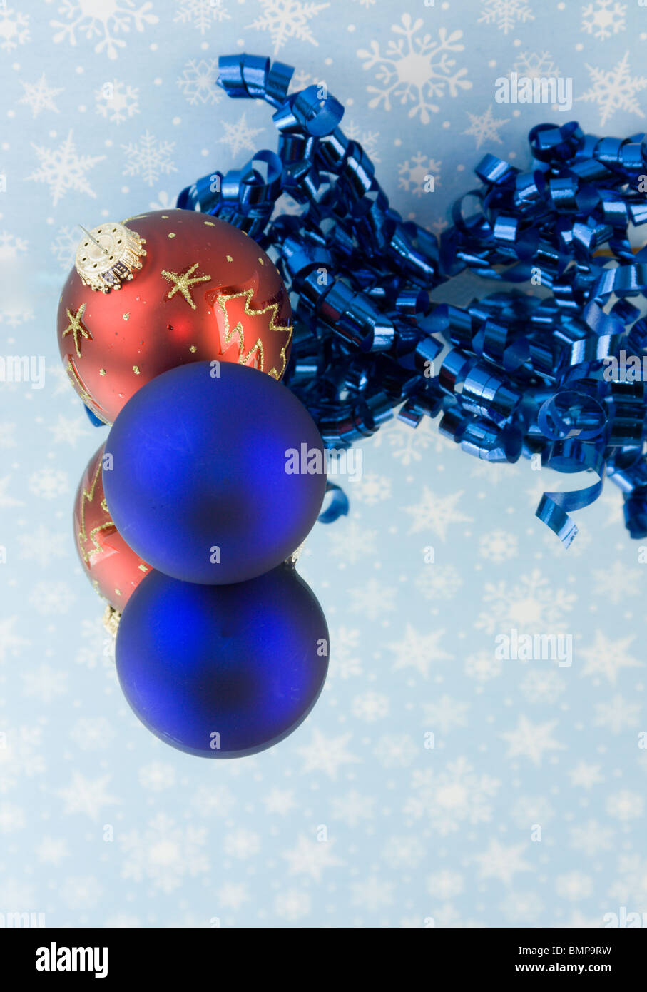 two Christmas baubles with curly ribbon on blue snowflake background Stock Photo