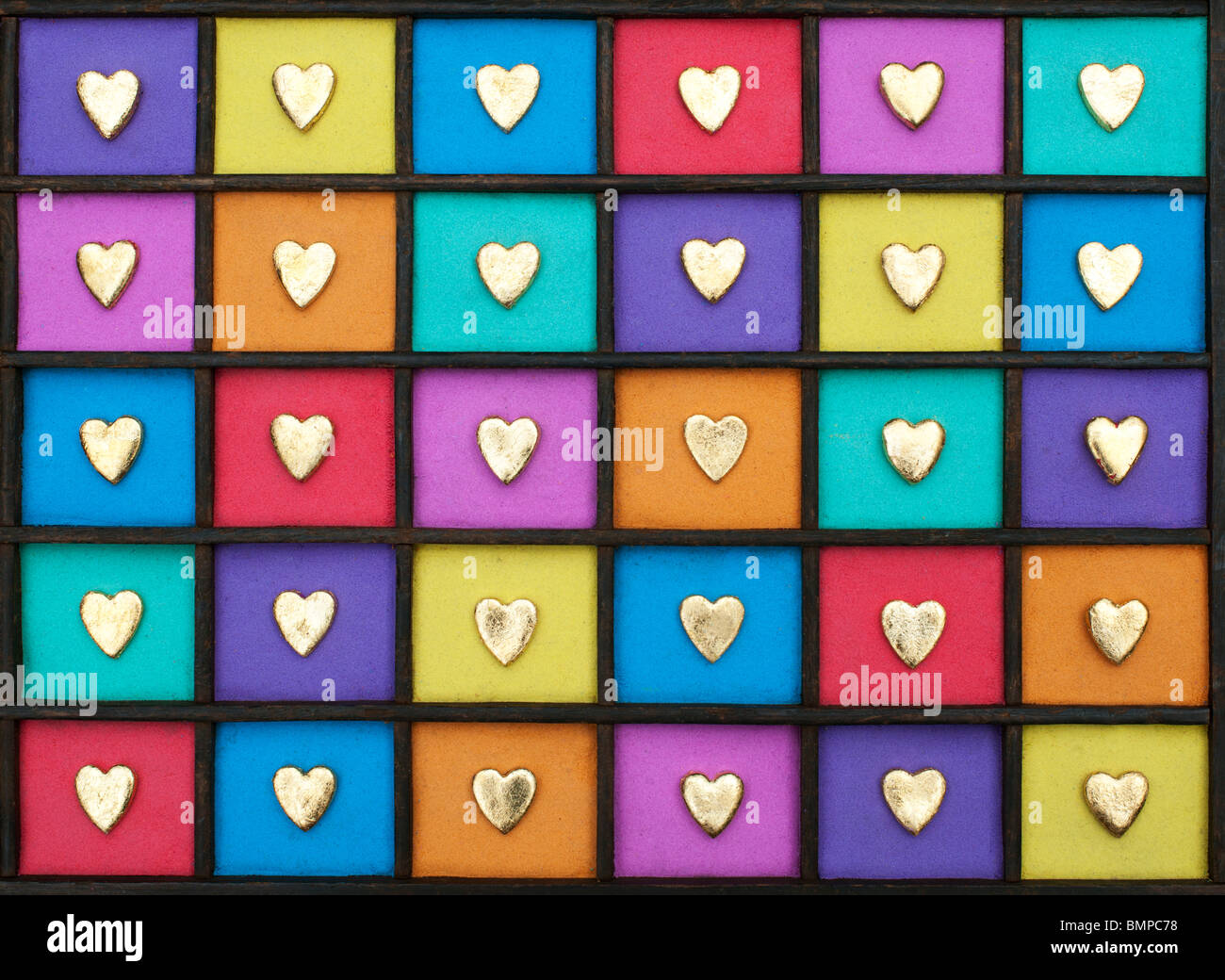 Multicoloured gold heart shape grid pattern in a wooden tray Stock Photo