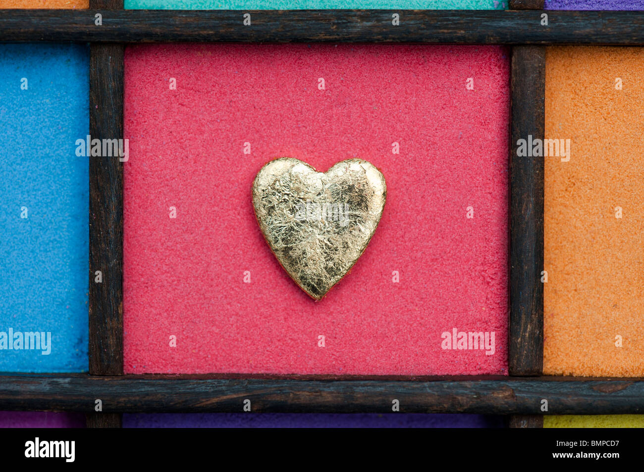 Gold heart shape against red sand in a wooden tray Stock Photo
