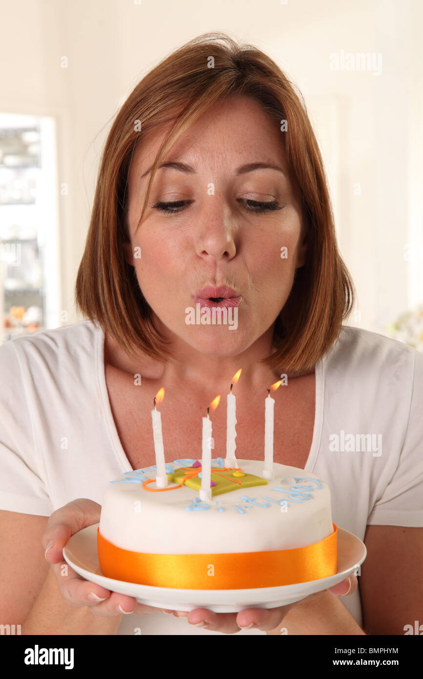 WOMAN BLOWING OUT CANDLES ON BIRTHDAY CAKE Stock Photo