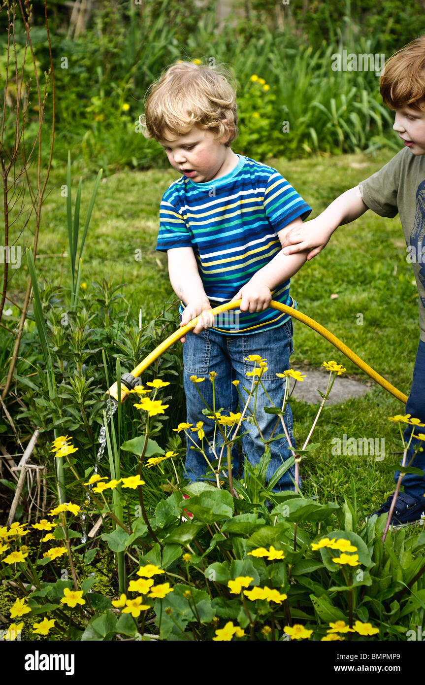 Two young brothers in a garden filling a pond with water using a yellow