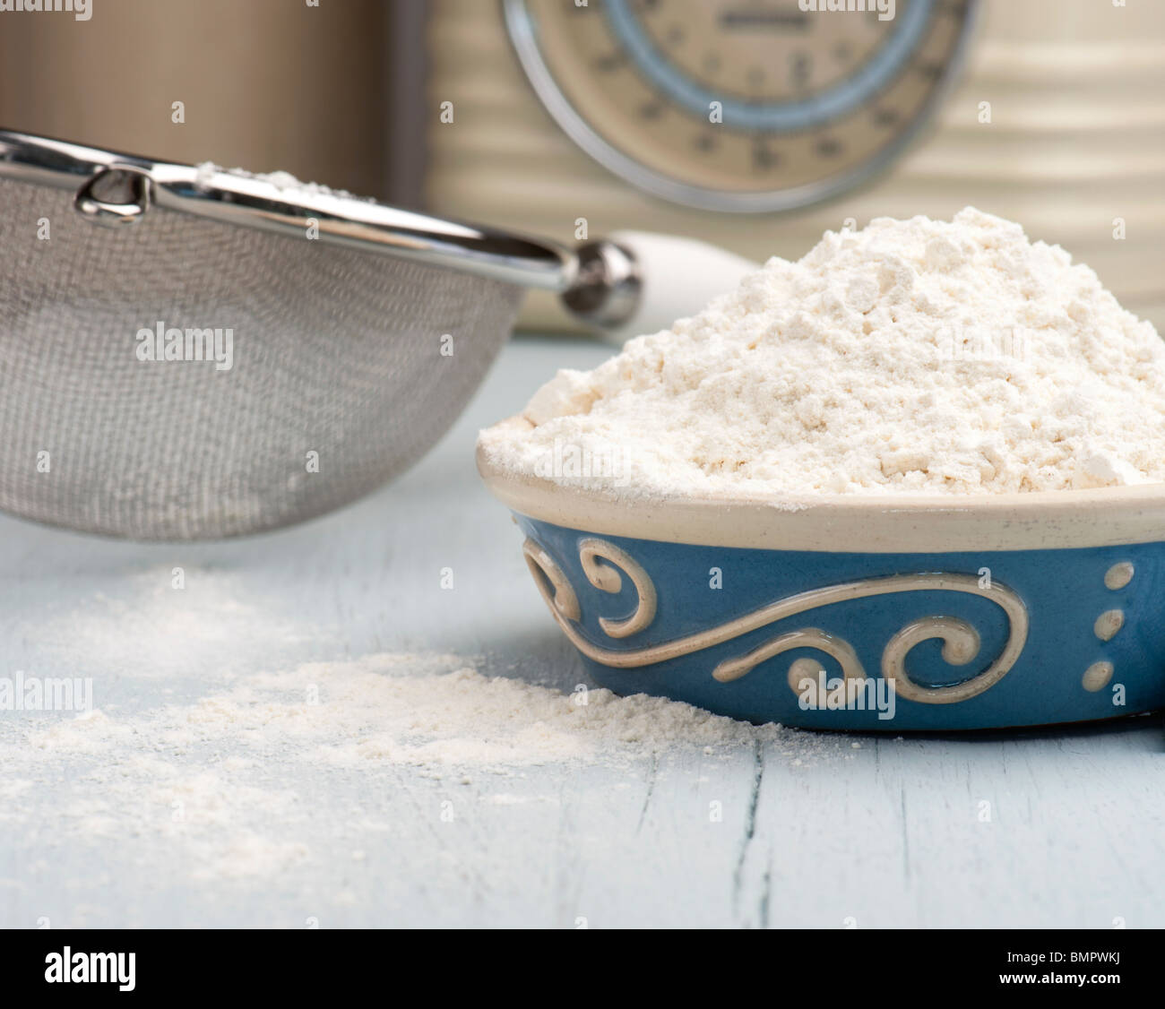 A Dish Full Of Flour With A Sieve and Scales In The Background Stock Photo
