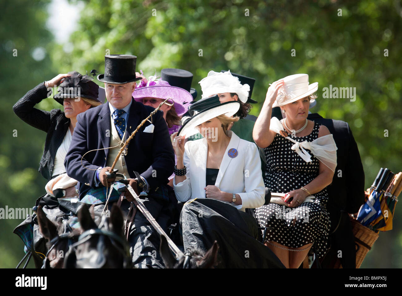 Race goers arrive by horse drawn carriage to the Royal Ascot race meeting wearing hats Stock Photo