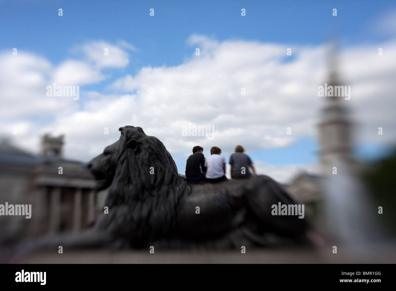 Three young men sitting on top of one of the lion statues in Trafalgar Square in London, England. Stock Photo