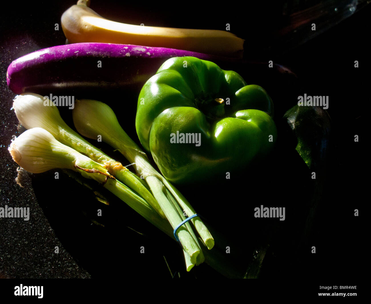 A banana, Japanese eggplant, green pepper,and a bunch of scallions form a still life in afternoon sun. Stock Photo