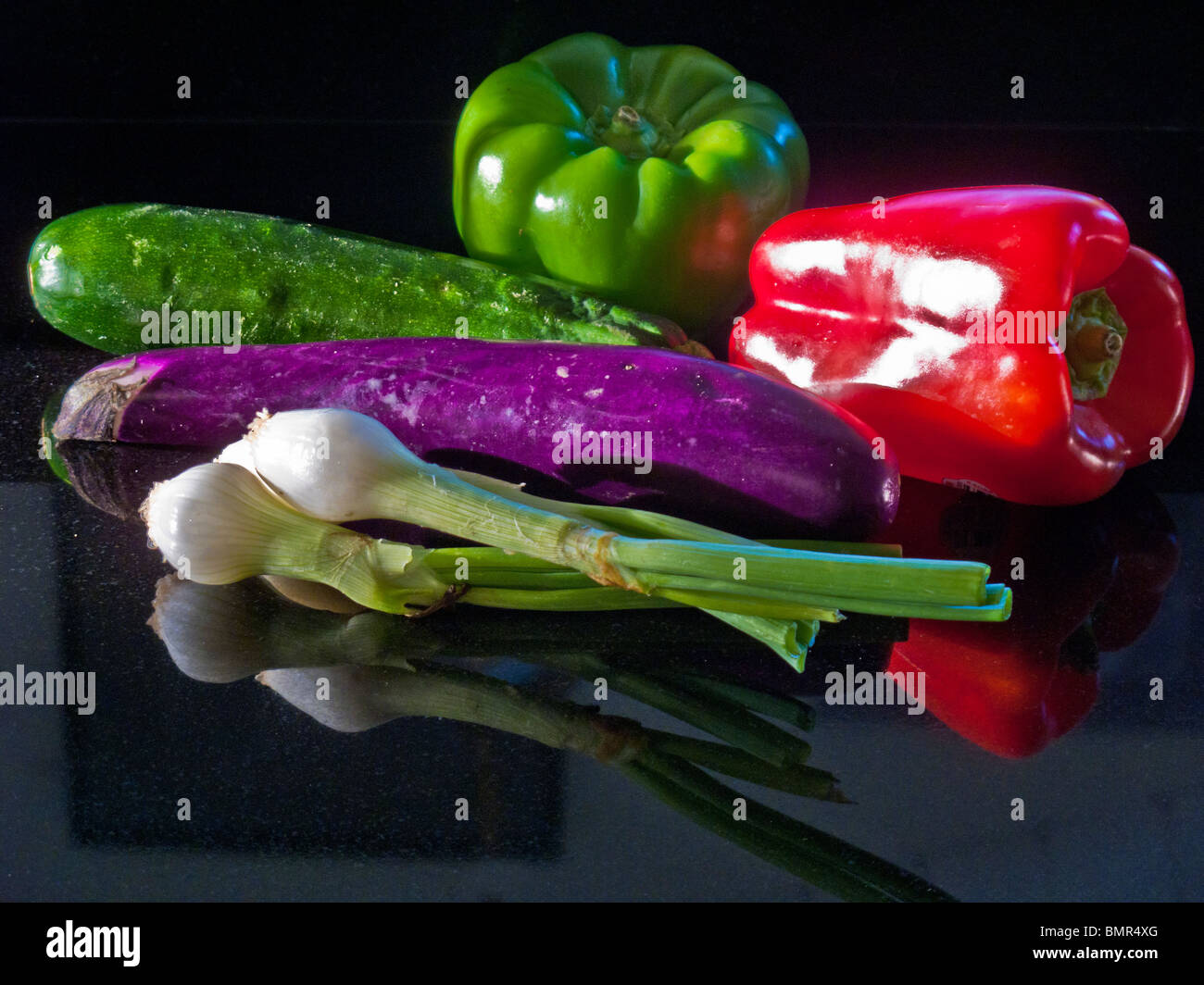 A Japanese eggplant, zucchini squash, green and red peppers, and a bunch of scallions form a still life in afternoon sun. Stock Photo