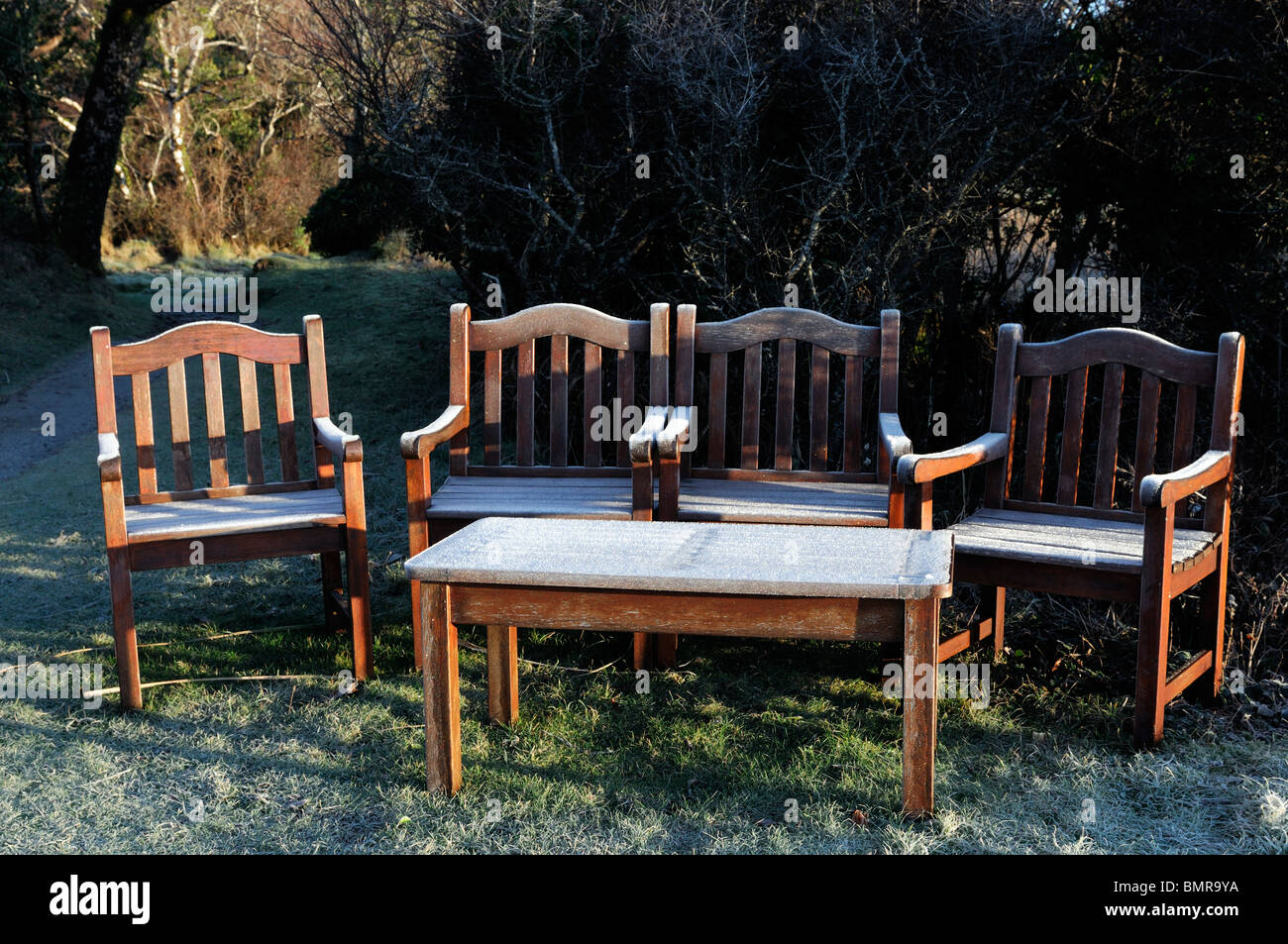 ice frost covered garden furniture wooden seat bench winter cold hedge seat chairs table seating early morning light sunrise Stock Photo