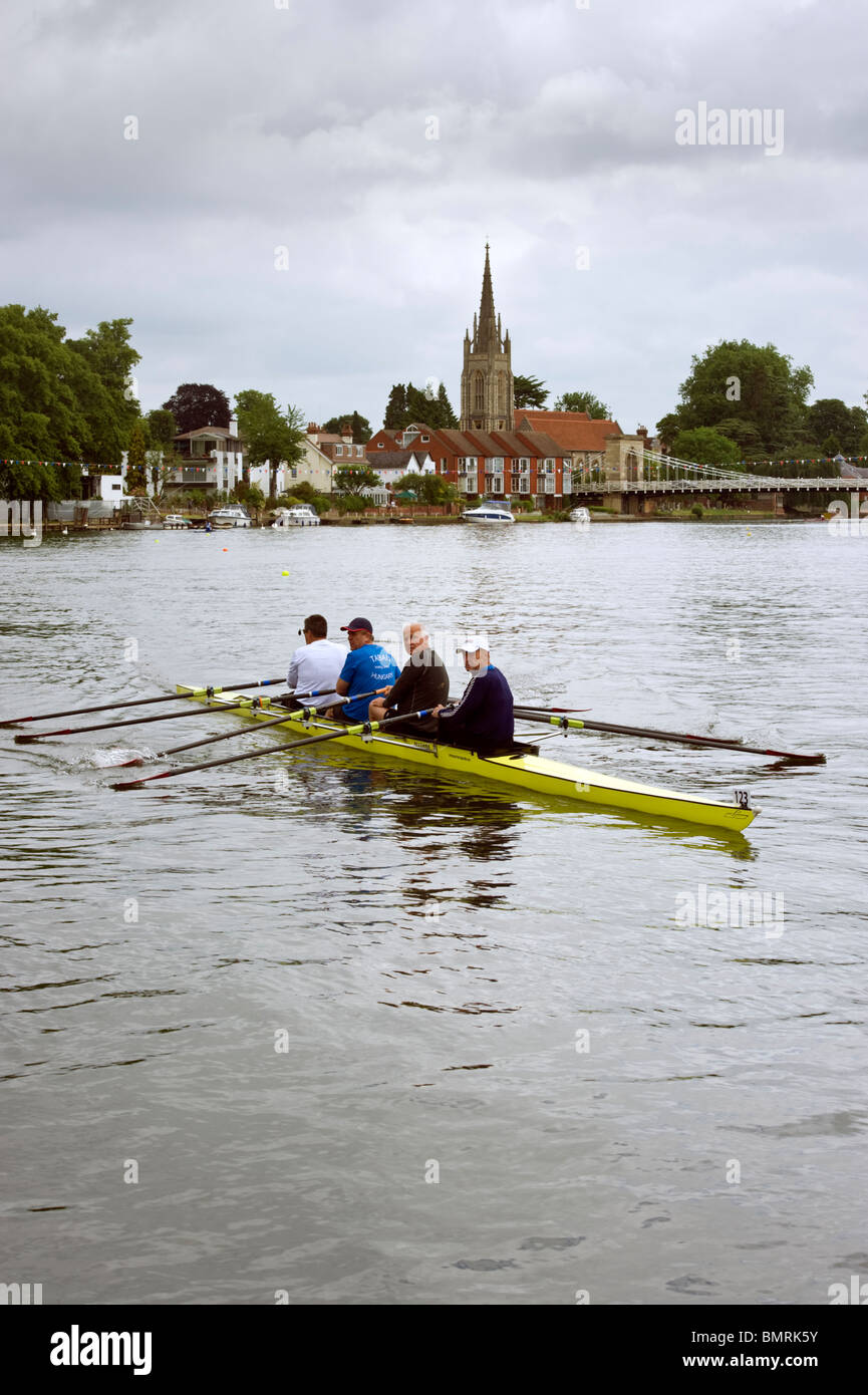 Four rowers in a skiff rowing upstream on the river Thames with All Saints church Marlow in the distance Stock Photo