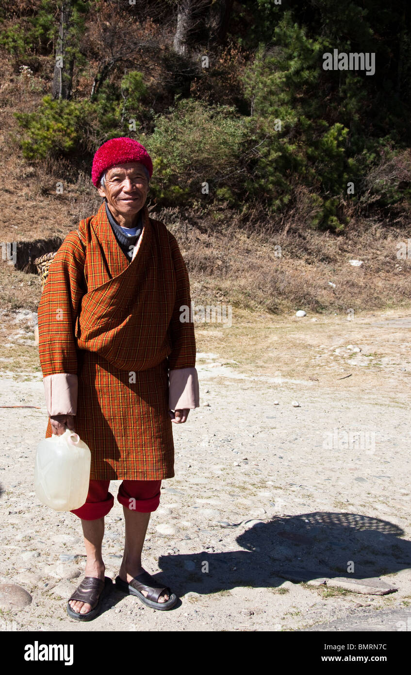 Old man in gho dress holding water can, Bumthang Bhutan Stock Photo