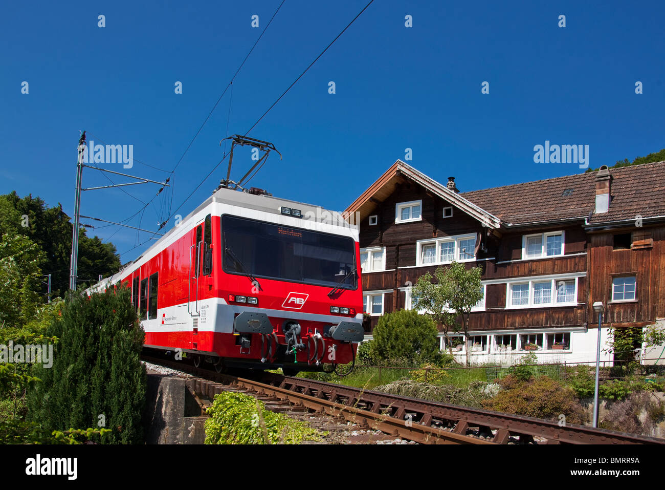 Appenzeller Bahnen local train passing by typical local farmhouse, Heiden Switzerland Stock Photo