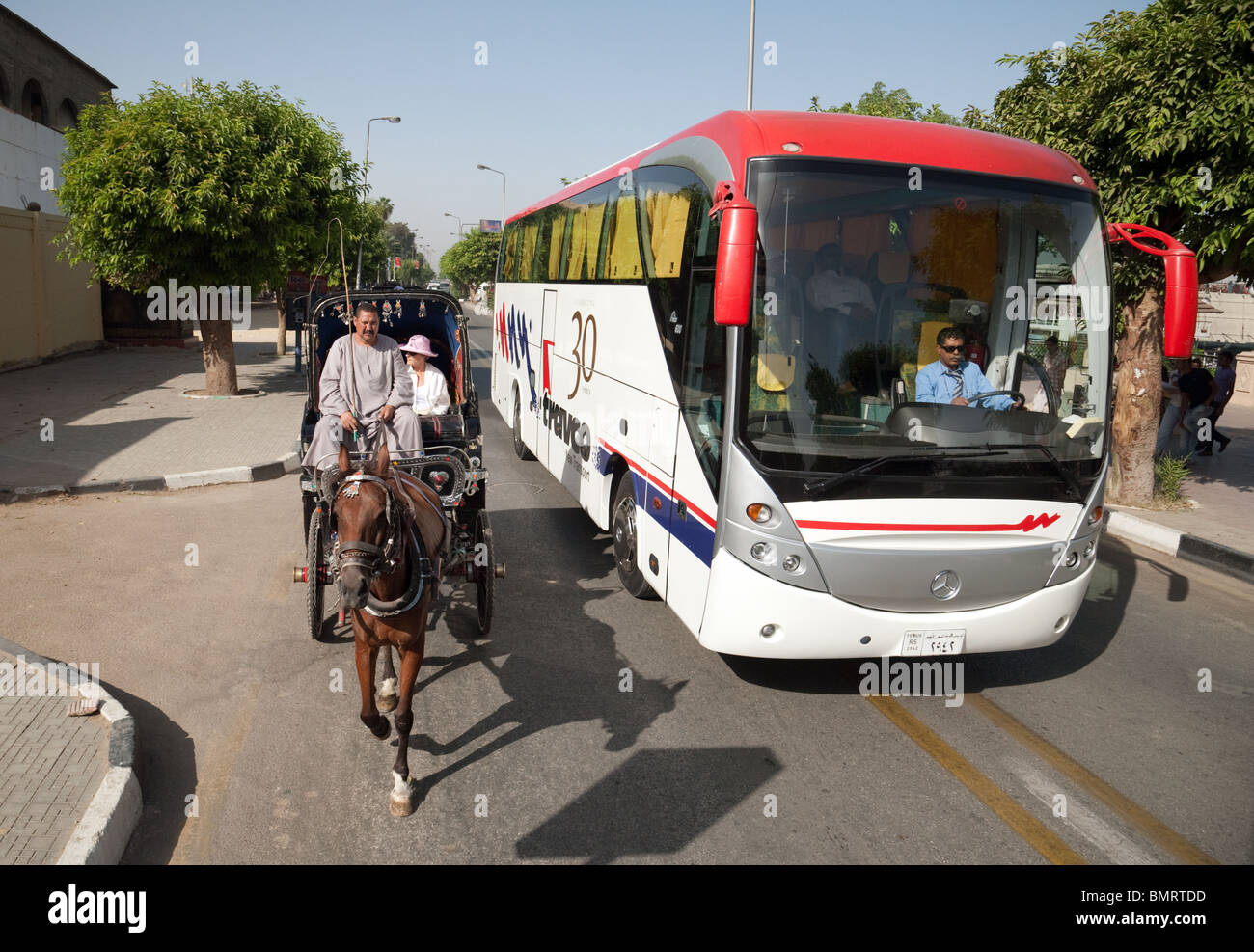 A modern tourist coach passes tourists in a traditional horse and carriage (Hantoor), Luxor, Upper Egypt Stock Photo