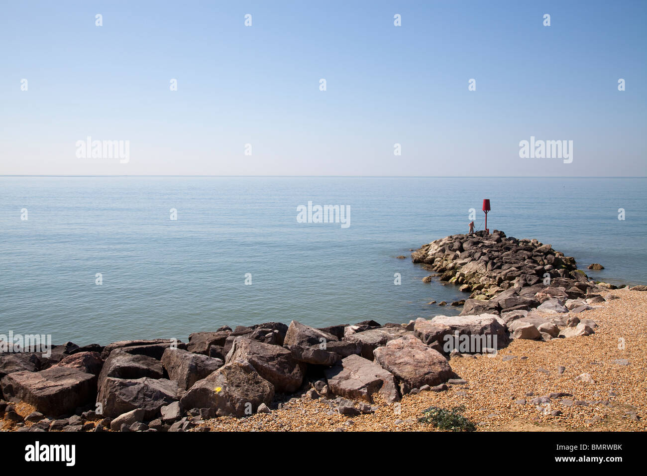 one man fishing off Rock stone groynes sea defences at Barton on Sea Stock Photo