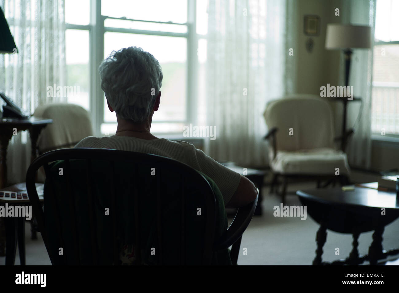 Old woman from behind as she sits looking out window. Stock Photo