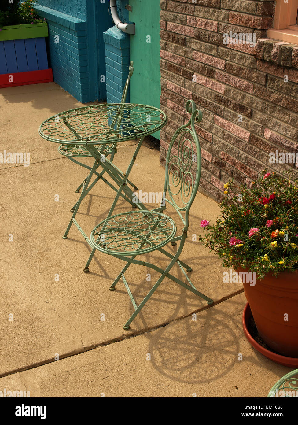 metal outdoor furniture table chairs green wire on cement patio before brick wall Stock Photo