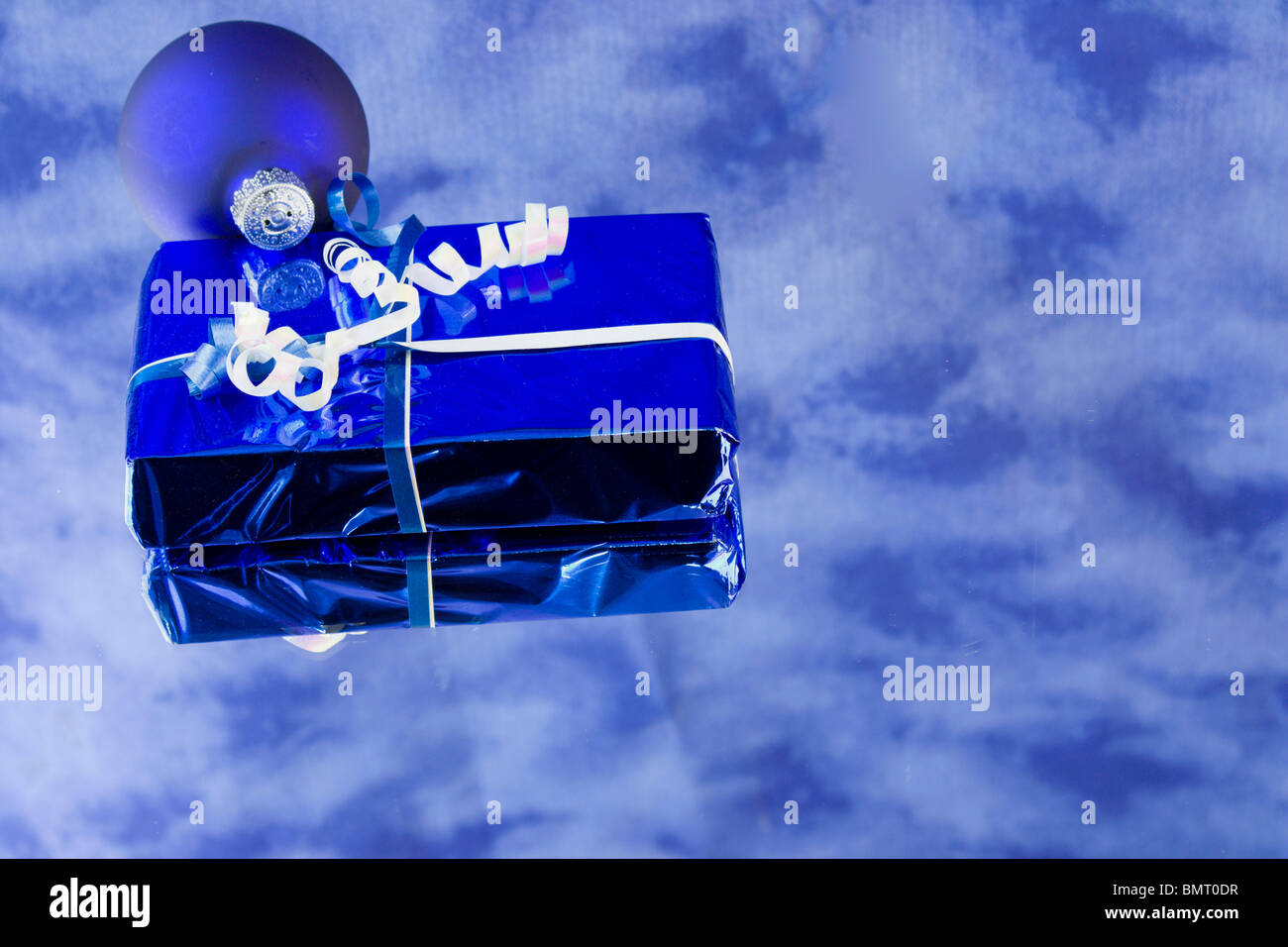 Blue foil wrapped Christmas present with bauble, reflections, and copyspace Stock Photo