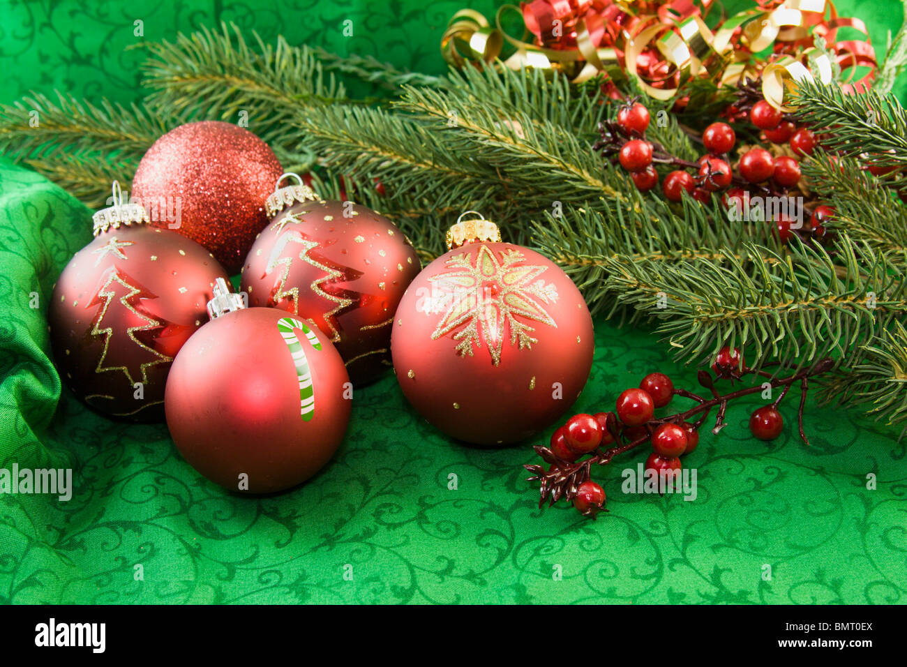red Christmas ornaments on a green background with fir branch and holly accents Stock Photo